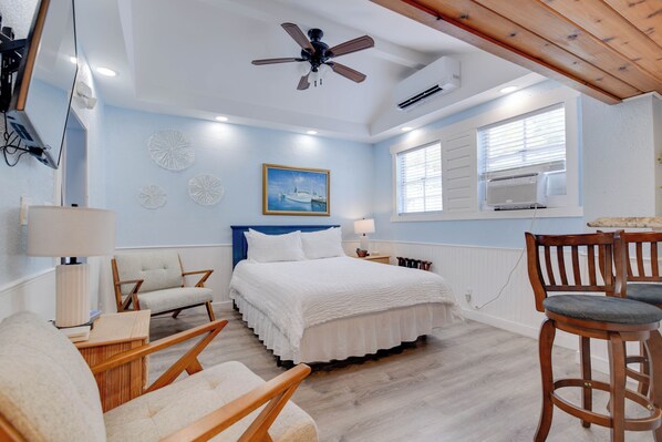 Ein Schlafzimmer mit einem Bett, zwei Stühlen, einem Schreibtisch, einem Deckenventilator und einem Fenster mit Jalousien.