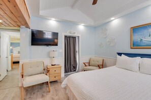 Une chambre à coucher avec un lit, deux chaises, un bureau avec une lampe, une télévision et un tableau accroché au mur.