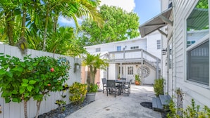 A patio with a table and chairs, surrounded by potted plants and a white fence. - Welcome Matt's - Truman @ Duval | Perfect Hideaway! (Key West)