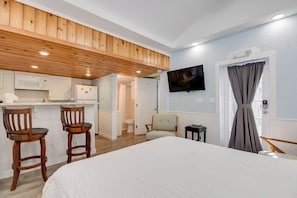 A bedroom with a bed, wooden ceiling, a TV, and a bathroom visible in the background. - Welcome Matt's - Truman @ Duval | Perfect Hideaway! (Key West)