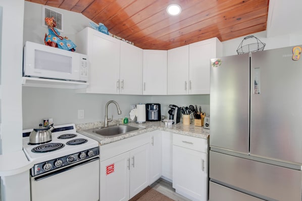 Una cocina con armarios blancos, un refrigerador de acero inoxidable, una estufa y un microondas.