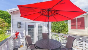A deck with a round table and four chairs, a red umbrella, and a white railing. - Jerry's Escape - Truman @ Duval | Cozy Studio, Perfect Location! (Key West)