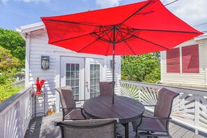 A deck with a round table and four chairs, a red umbrella, and a white railing.