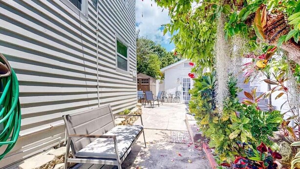 Un patio con un banco, una manguera y un muro de jardín con diversas plantas.