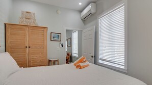 Un dormitorio con una cama grande, un armario, un equipo de aire acondicionado, una puerta que da a otra habitación y una ventana con persianas.