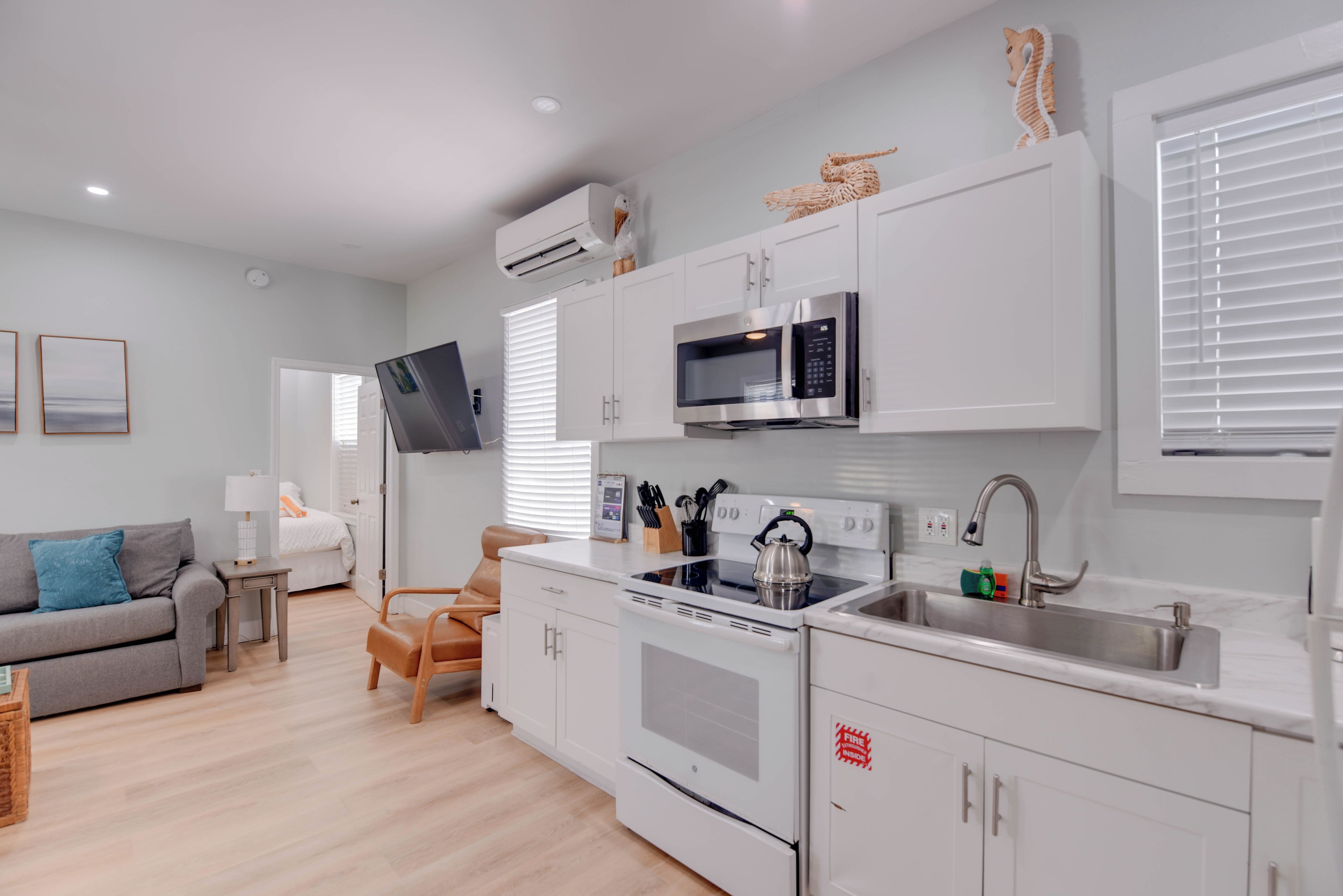 A modern kitchen with white cabinetry, a built-in microwave, a kettle, and a stainless steel sink.