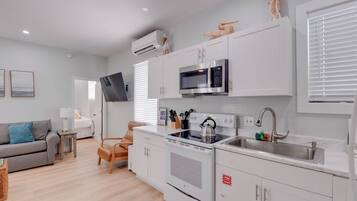 A modern kitchen with white cabinetry, a built-in microwave, a kettle, and a stainless steel sink.