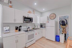 Une cuisine moderne avec des meubles blancs, un four à micro-ondes en acier inoxydable, une bouilloire et un réfrigérateur.