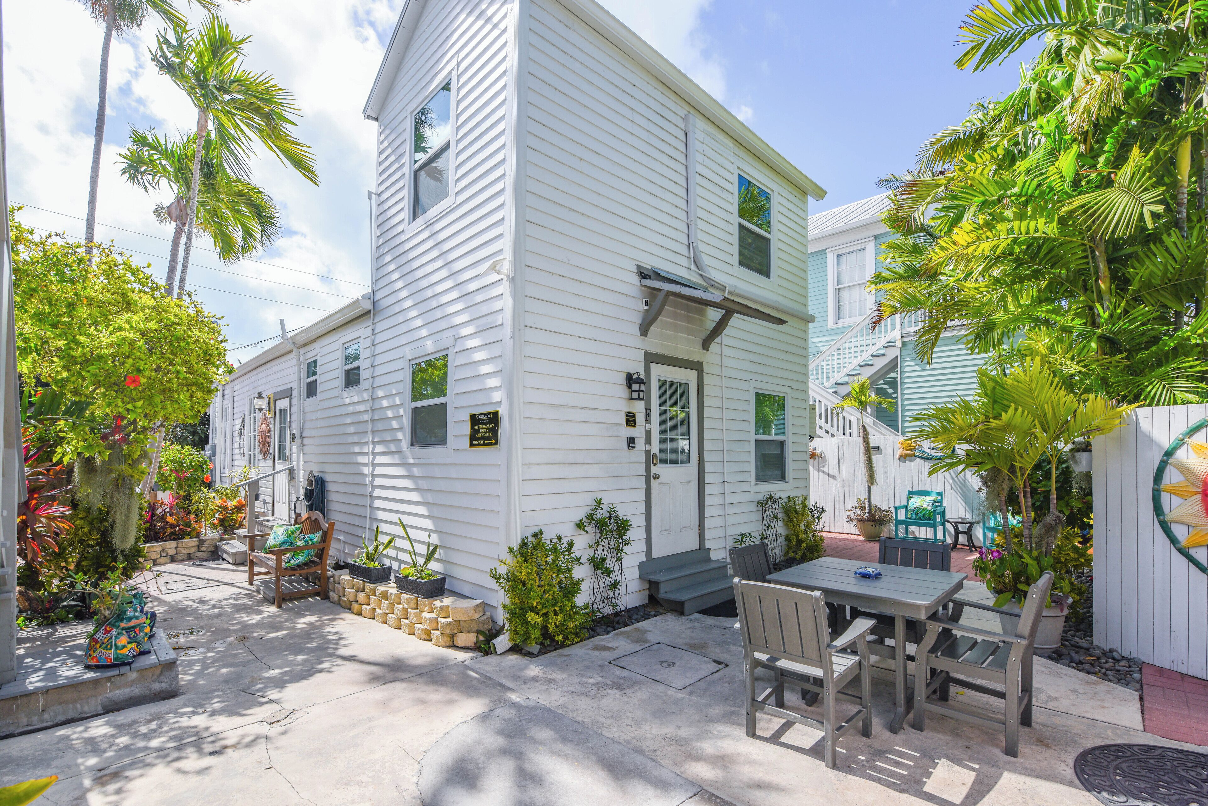 A white two-story house with a patio, outdoor seating, and tropical plants.