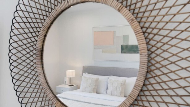 A bedroom with a bed, nightstand, lamp, and a wall-mounted mirror with a geometric frame. - Augustus Hideaway Studio Apt with Air-Con (Auckland Central Suburbs)