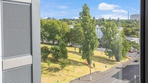 A view from a window overlooking a grassy area with trees and a road. - Augustus Hideaway Studio Apt with Air-Con (Auckland Central Suburbs)