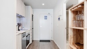 A narrow kitchen with white cabinets, a built-in oven, and a wooden shelf with glassware. - Augustus Hideaway Studio Apt with Air-Con (Auckland Central Suburbs)