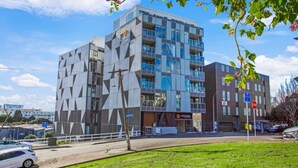 A modern building with a geometric facade, a visible entrance, and a parking area with cars. - Augustus Hideaway Studio Apt with Air-Con (Auckland Central Suburbs)
