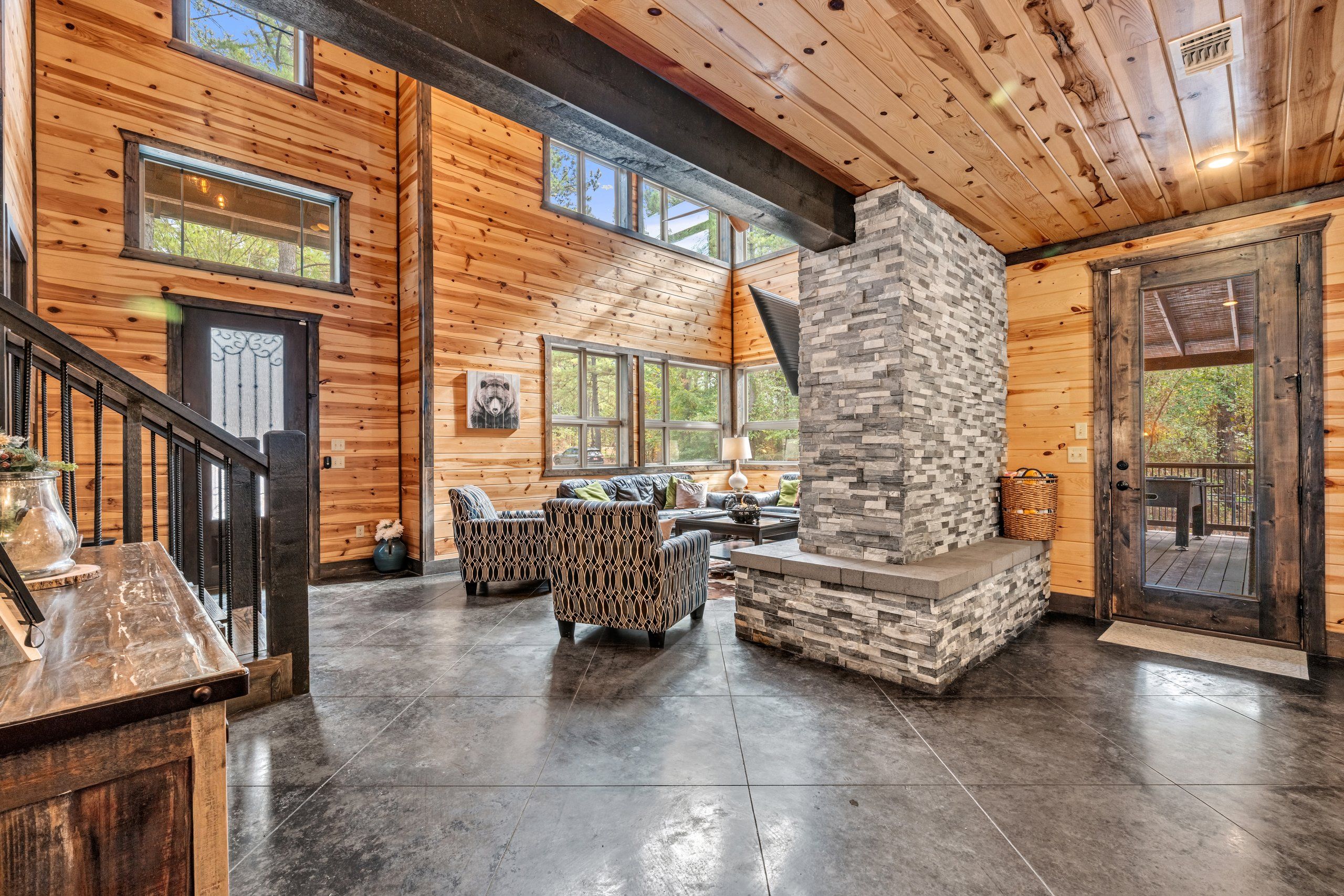 Un intérieur spacieux avec une cheminée en pierre, des murs en bois et une grande fenêtre donnant sur une forêt.