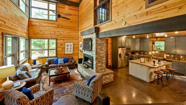 Ein geräumiges Holzblockhaus-Interieur mit zentralem Kamin, einer Küchenzeile und einer Sitzecke mit mehreren Sofas und einem Couchtisch.