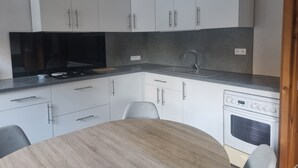 A modern kitchen with white cabinets, a grey countertop, a sink, a stove, and a dining table with chairs. - 2-bedroom apartment LA GIETTAZ 4 km from the ski slopes with free shuttle service (La Giettaz)