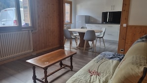 A cozy room with a wooden bench, a sofa, a dining table with chairs, and a kitchen area with cabinets and a refrigerator. - 2-bedroom apartment LA GIETTAZ 4 km from the ski slopes with free shuttle service (La Giettaz)