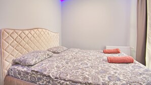A bedroom with a tufted headboard, a patterned bedspread, and two rolled towels. - Aparton.by - Makaenka 12G-1x6 str. (Minsk)