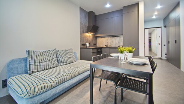 A modern living room with a sofa, dining table, chairs, and a kitchen area. - Aparton.by - Makaenka 12G-1x6 str. (Minsk)