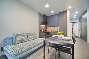 Een moderne woonkamer met een bank, eettafel, stoelen en een keukenhoek.