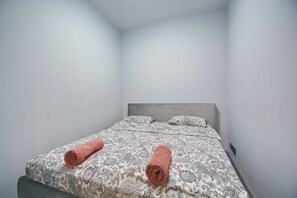 Een eenpersoonsbed met een bedsprei met dessin en twee opgerolde handdoeken.