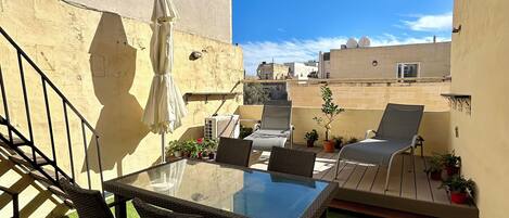 En tagterrasse med et glasbord, fletstole, parasol og plantekasser.