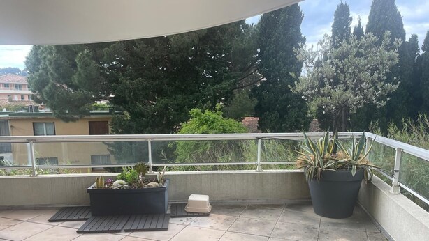 Un balcon avec un sol carrelé, des plantes en pot et une balustrade.