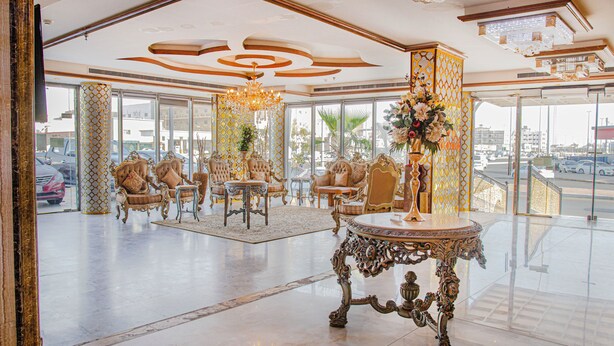 A spacious lobby with ornate furniture, a chandelier, and large windows offering a view of the street.