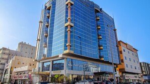 A modern high-rise building with a glass facade, multiple balconies, and commercial spaces on the ground floor.