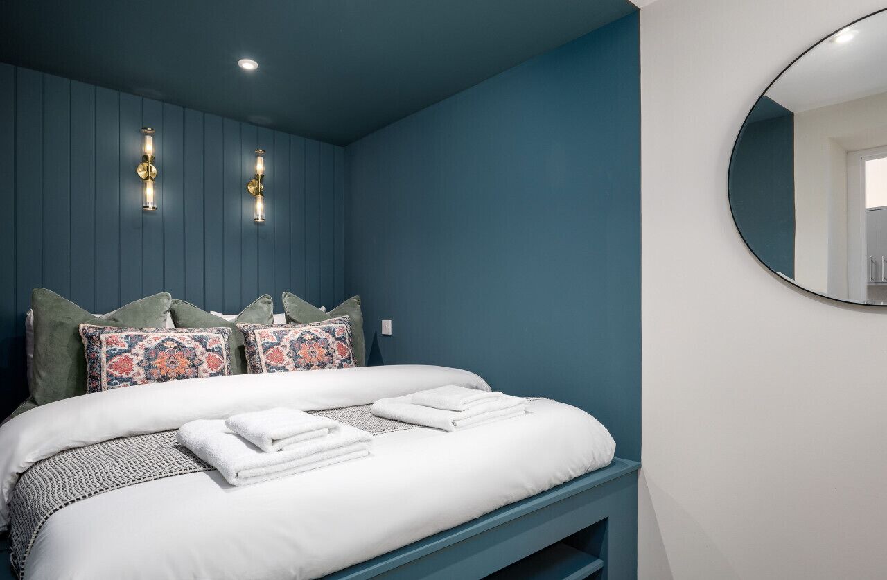 Une chambre à coucher avec un lit, des oreillers, un miroir rond et des appliques murales.