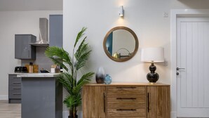 A modern kitchen with a grey countertop, a wooden cabinet, a round mirror, and a potted plant.
