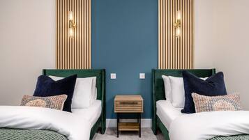 Una stanza con due letti, un piccolo comodino di legno e illuminazione a parete.