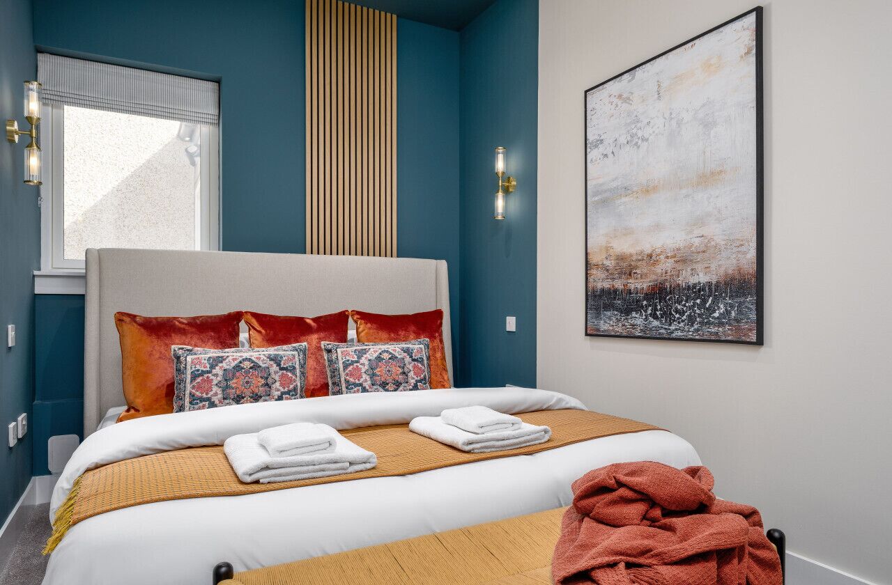 Une chambre à coucher avec un lit, des oreillers, une couverture, une fenêtre et un tableau accroché au mur.