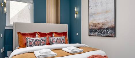 A bedroom with a bed, pillows, a blanket, a window, and a painting on the wall.