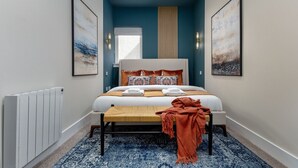 A bedroom with a bed, a bench, a radiator, and two wall-mounted light fixtures.