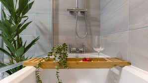 A bathtub with a wooden shelf, a glass of water, and a plant.