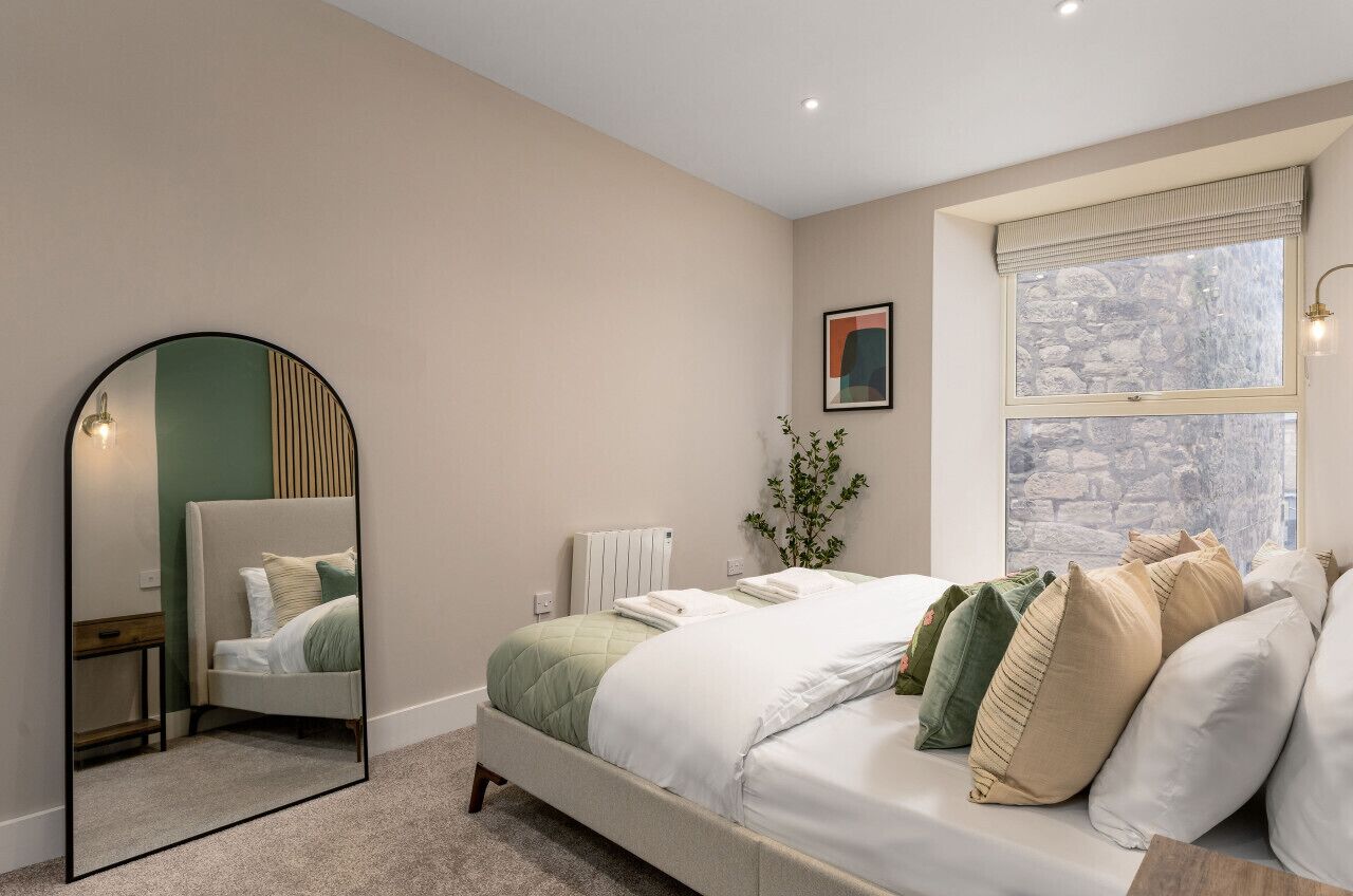 Een slaapkamer met een bed, een spiegel, een radiator, een raam met uitzicht en een plant.