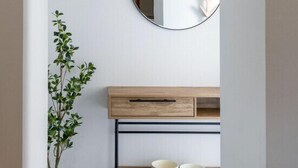 Een gang met een houten console tafel, een ronde spiegel en een potplant.