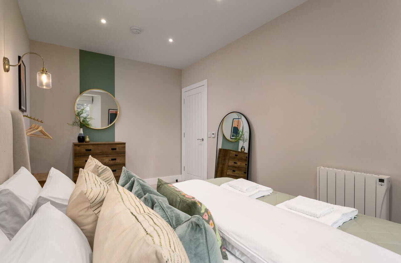 A bedroom with two beds, a dresser, a mirror, and a radiator.
