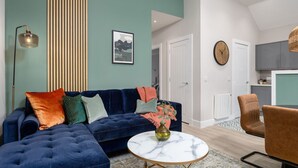 Een moderne woonkamer met een blauwe modulaire bank, een ronde salontafel en een keuken op de achtergrond.