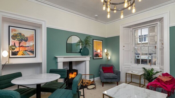 Ein gemütliches Wohnzimmer mit Kamin, grünen Polstersesseln, einem Marmortisch und Kunstwerken an den Wänden.