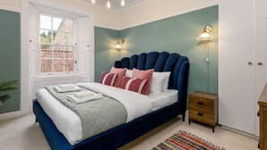 Ein Schlafzimmer mit Bett, Nachttisch, Lampe und Blick durch ein Fenster.