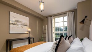 Une chambre à coucher avec un lit, une table de chevet avec une lampe, une fenêtre avec des rideaux et un tableau accroché au mur.