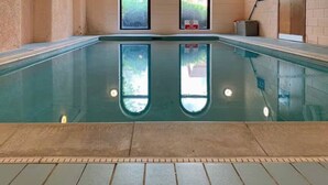 Une piscine intérieure avec des parois en verre transparent, un sol carrelé et une petite fenêtre sur laquelle est apposée une pancarte.