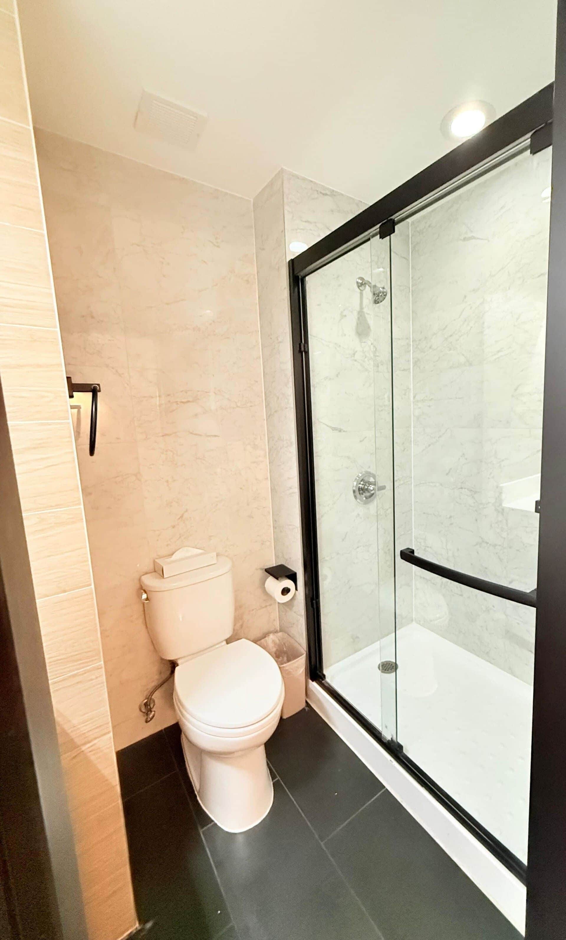 Un baño moderno con inodoro, cabina de ducha de vidrio y pared revestida de mármol.