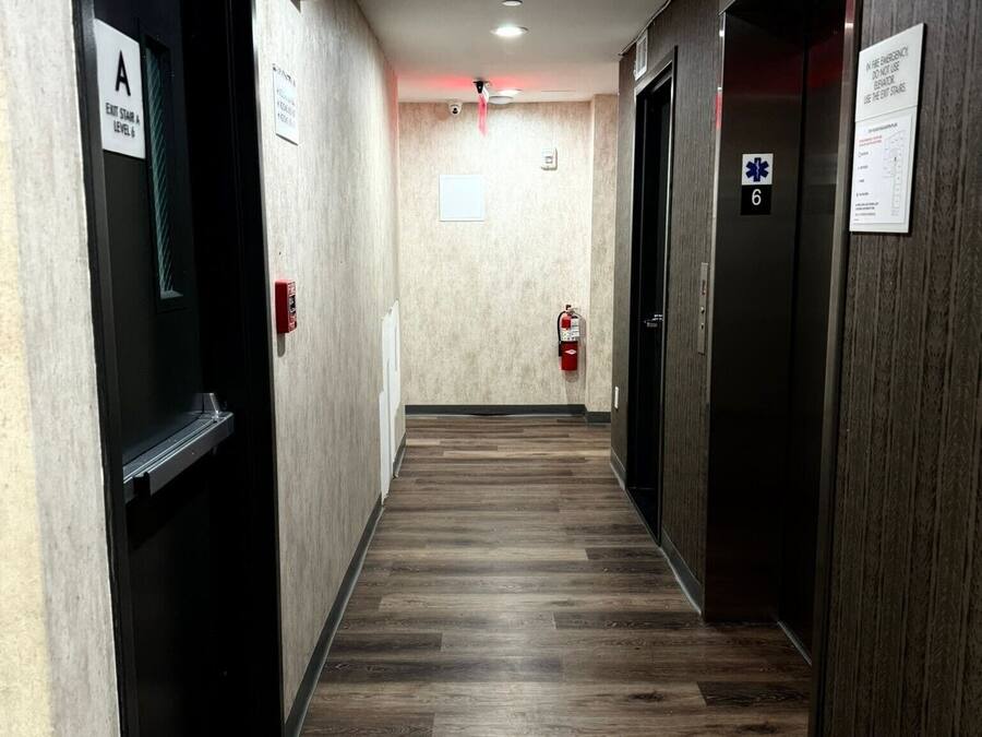 A hallway with wooden flooring, emergency exit signs, and fire extinguishers.