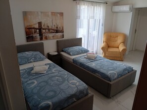 Quarto com duas camas, uma cadeira e um quadro de uma ponte.