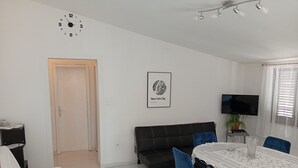 Una sala de estar moderna con un sofá, una mesa de comedor con sillas, un televisor y un reloj en la pared.