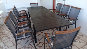 Una mesa rectangular con ocho sillas, cada una con respaldo de malla y apoyabrazos de madera. El suelo está cubierto de baldosas con un diseño geométrico.