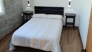 Un dormitorio con una cama grande, dos mesitas de noche con lámparas, una pared de piedra y suelo de madera.